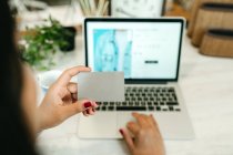 Обрізати невпізнавану жінку, роблячи покупки з пластиковою карткою для замовлення під час онлайн-покупки через ноутбук — стокове фото