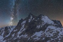 Захватывающий вид галактики в небе с межзвездным газом над грубой величественной горой с снегом вечером — стоковое фото