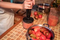 Анонимная домохозяйка, смешивающая помидоры в блендере во время приготовления соуса маринара на кухне дома — стоковое фото