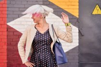 Alternative insouciante femelle jetant les cheveux courts teints contre un mur coloré en zone urbaine — Photo de stock