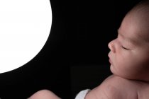 Vista laterale del tenero neonato che dorme sul letto e tocca la lampada luminosa luminosa notturna nella stanza buia — Foto stock