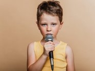 Cool child in singing in modern mic on brown background in studio — Stock Photo