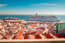 Moderne Schiffe ankern im Kreuzfahrthafen Lissabon in der Nähe von Häusern mit roten Ziegeldächern vor blauem Himmel an sonnigen Tagen in Portugal — Stockfoto