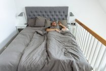 Сверху мирный мужчина лежит в мягкой постели под одеялом и спит утром в спальне — стоковое фото