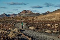 Anonymous hiker with backpack walking on dry path in valley near hills on cloudy summer day in Fuerteventura, Spain — Stock Photo
