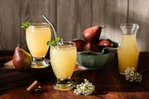Gläser mit köstlichen Erfrischungsgetränken mit Birnensaft und frischen Holunderblütenblättern auf dem Tisch mit Zimtstangen — Stockfoto