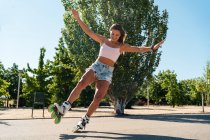 Young fit female in rollerblades showing stunt on road in city in summer — Stock Photo
