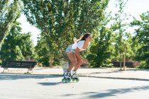 Side view of fit female in rollerblades showing stunt on road in city in summer — Stock Photo