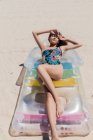 Сверху счастливая женщина в купальнике лежит на надувном матрасе на песчаном берегу моря и загорает в солнечный день во время летних каникул — стоковое фото