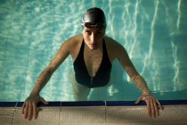 Молода красива жінка в критому басейні, одягнена в чорний купальник, дивиться на камеру — стокове фото