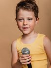Холодный ребенок в пении в современном микрофоне на коричневом фоне в студии — стоковое фото
