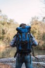 Мужчина турист с рюкзаком стоит на озере в лесу и смотрит в сторону — стоковое фото