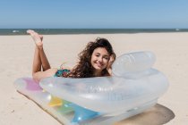 Vista lateral da fêmea feliz em maiô deitado no colchão inflável na praia arenosa e banho de sol no dia ensolarado durante as férias de verão — Fotografia de Stock