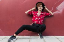 Trendy homosexual man with long nails in ornamental shirt looking at camera while squatting on pavement against wall — Stock Photo