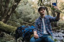 Zufriedener männlicher Wanderer mit Rucksack macht unterwegs Selfie — Stockfoto