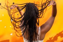 Vista posterior de una hembra afroamericana irreconocible lanzando largos cabellos trenzados sobre un fondo amarillo vivo en Barcelona - foto de stock