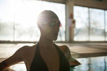Jovem mulher bonita no passeio da piscina interior, com maiô preto, raios de sol entrando pela janela — Fotografia de Stock