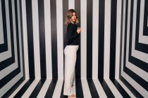 Young seductive woman in white trousers and black jacket looking at camera on striped floor — Stock Photo