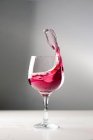 Cold alcohol red drink splashing out of glass goblet on grey background in studio — Stock Photo