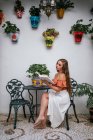 Donna graziosa in gonna gambe appoggiate sulla sedia mentre si rilassa in patio in estate e godersi la storia interessante nel libro durante il fine settimana — Foto stock