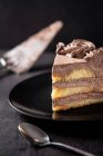 De cima de pedaço de delicioso bolo de chocolate trufa servido em prato na mesa preta com colher e espátula — Fotografia de Stock
