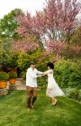 Pareja multirracial optimista tomados de la mano y bailando en el césped mientras se divierten en el jardín de verano - foto de stock