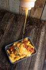 Molho de queijo derramando no prato com batatas fritas apetitosas e pimentas picantes colocadas em mesa de madeira no restaurante — Fotografia de Stock