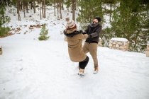 Восхитительная пара в теплой одежде, держась за руки и кружась в снежных зимних лесах, веселясь — стоковое фото