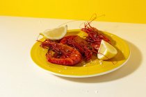 Tasty seafood of cooked red shrimps with fresh lemon slices and coarse salt on two color background — Stock Photo