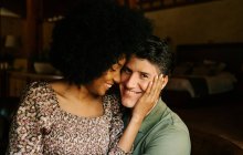 Dall'alto di amare la donna nera seduta sulle ginocchia dell'uomo mentre abbraccia a casa — Foto stock