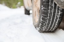 Ground level of tire of wheel of automobile parked on snowy roadway in winter forest — Stock Photo