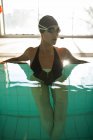 Joven hermosa mujer en la acera de la piscina cubierta, con traje de baño negro, rayos de sol que entran por la ventana - foto de stock