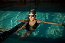 Joven hermosa mujer dentro de la piscina cubierta, con un traje de baño negro y la celebración de la barcaza de natación - foto de stock