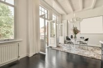 Modern loft home interior design with dining table and chairs placed near window in corner of spacious room with mockup pictures hanging on white wall in house — Stock Photo