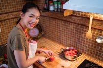 Dall'alto femmina etnica in grembiule tagliando pomodori maturi sul tagliere mentre si cucina il pranzo in cucina a casa — Foto stock