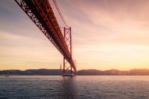 D'en bas poteaux d'amarrage métalliques rouillés situés sur la rive du Tage sous le pont 25 de Abril au coucher du soleil à Lisbonne, Portugal — Photo de stock