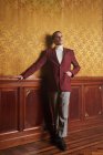 Впевнений дорослий чоловік-актор в елегантному стильному одязі тримає руку в кишені і задумливо дивиться, стоячи біля стіни в старовинному стилі кімнати — стокове фото