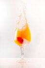Refrescante cóctel naranja salpicando en copa de vidrio brillante sobre fondo gris en el estudio - foto de stock