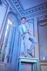 From below of expressive happy male in stylish suit balancing on table in posh room with blue neon light looking away — Stock Photo