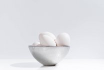 Миска зі свіжими курячими яйцями, розміщеними на столі на білому тлі в студії — стокове фото