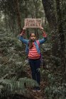Bambino etnico che solleva un pezzo di cartone con l'iscrizione Save The Planet mentre guarda la fotocamera nella foresta verde — Foto stock