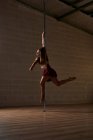 Seitenansicht einer anmutigen Tänzerin, die mit ausgestrecktem Arm an der Stange hängt, während sie im modernen Studio probt — Stockfoto