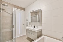 Interno della casa bagno con specchio appeso sopra doppio lavabo collocato vicino alla porta d'ingresso e cabina doccia in vetro in appartamento moderno — Foto stock