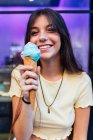 Crop allegro giovane femmina in ciondolo e orecchini con delizioso gelato in cono cialda guardando la fotocamera sulla strada — Foto stock