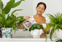 Charmante ethnische Frau gießt Wasser aus Krug in affenförmigen Topf mit Pflanze im Hausgarten — Stockfoto