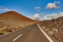 Autopista recta de asfalto que atraviesa el campo hacia el paseo de montaña por la mañana en Fuerteventura, España - foto de stock