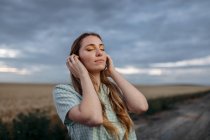 Стильна молода жінка з закритими очима торкається довгого волосся на проїжджій частині під хмарним небом в сутінках — стокове фото