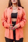 Обрізати невпізнавану жінку з барвистими довгими цвяхами в яскравій сорочці, що стоїть біля помаранчевої стіни — стокове фото