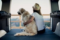 Irreconocible turista femenina abrazando obediente perro Golden Retriever acostado en el colchón dentro de autocaravana y admirando la naturaleza - foto de stock