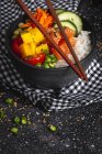 Alto ángulo de empuje asiático con salmón y arroz con verduras variadas servidas en tazón en la mesa con palillos en el restaurante - foto de stock